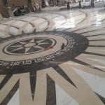 Full-scale marble floor medallion mock-up with a compass rose, Greek key border, and radial stone inlay.