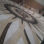 Full-scale marble floor medallion mock-up with a compass rose, Greek key border, and radial stone inlay.