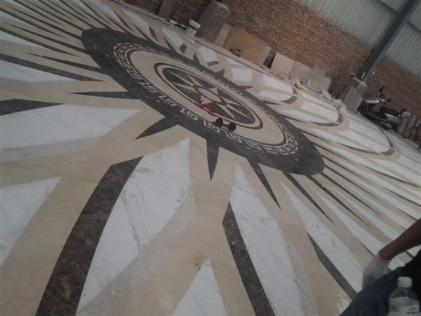 Full-scale marble floor medallion mock-up with a compass rose, Greek key border, and radial stone inlay.