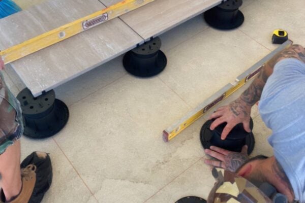 Installers use spirit levels to level porcelain pavers while adjusting Buzon slope correctors during pedestal system installation.