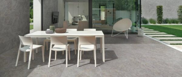 Marmo Gray porcelain pavers create a modern patio and dining area beside a luxury home with floor-to-ceiling glass walls and porcelain-clad walls.