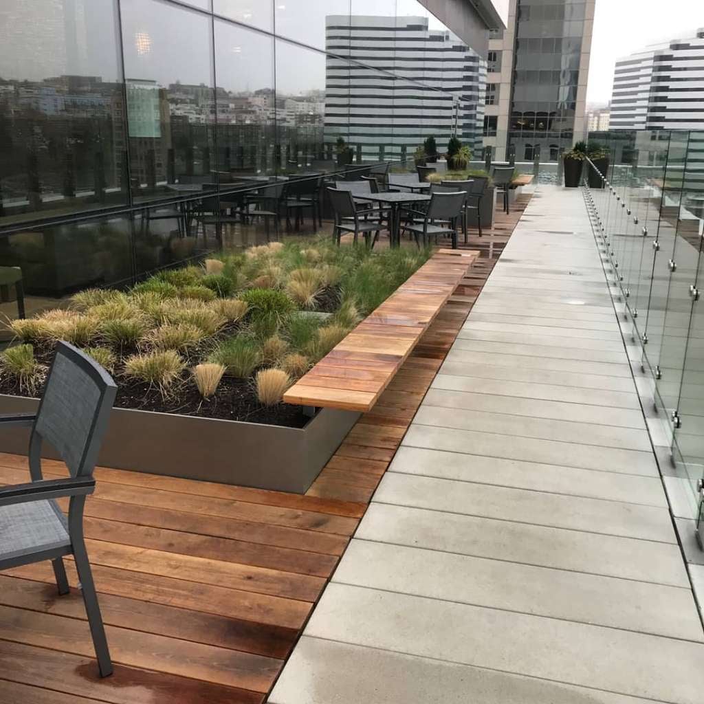 Hotel rooftop terrace featuring Black Locust decking, porcelain pavers, built-in wood benches, and glass railings.